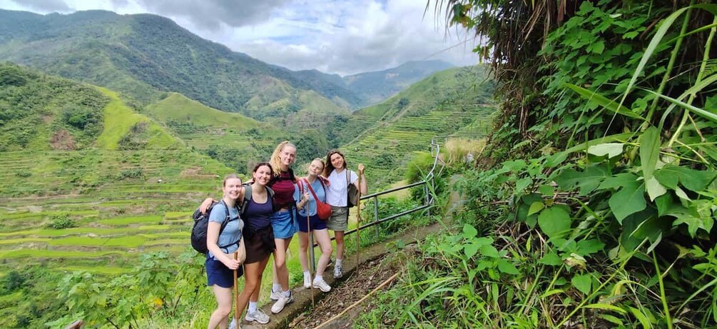 A group of hikers on a trail with lush green hills and a cloudy sky in the background. 2