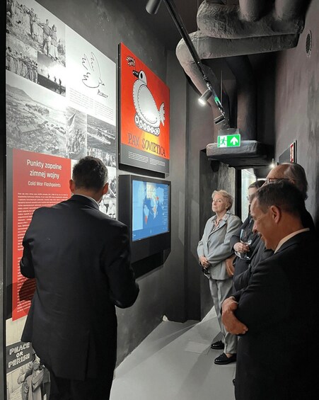 A group of people observing a display with historical photographs and a television screen. 2