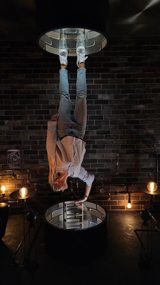 A person performing an acrobatic stunt on a circular platform in a dimly lit room with brick walls and hanging lights. 3