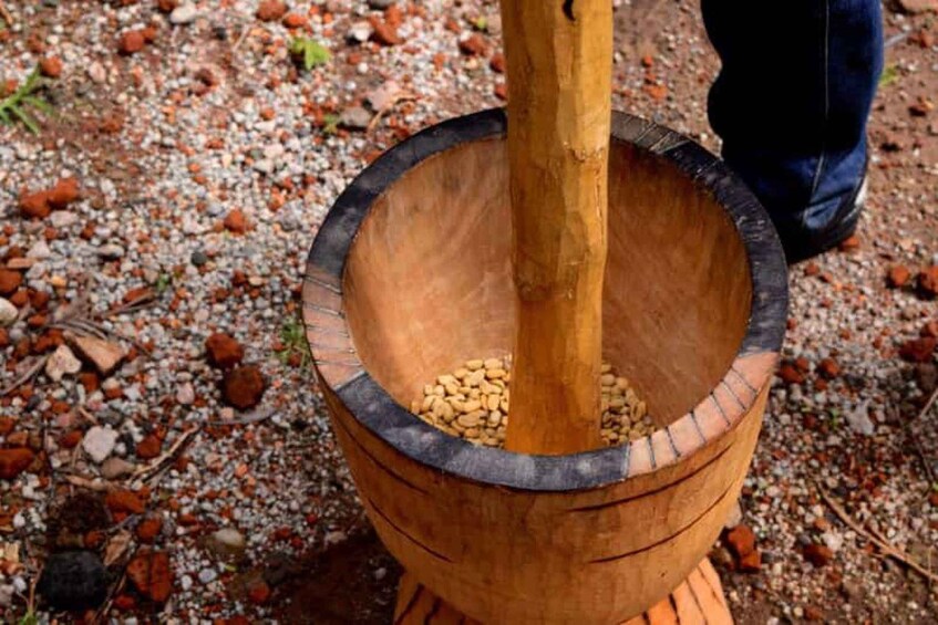 A wooden mortar with a pestle, filled with nuts, on a gravel surface. 1