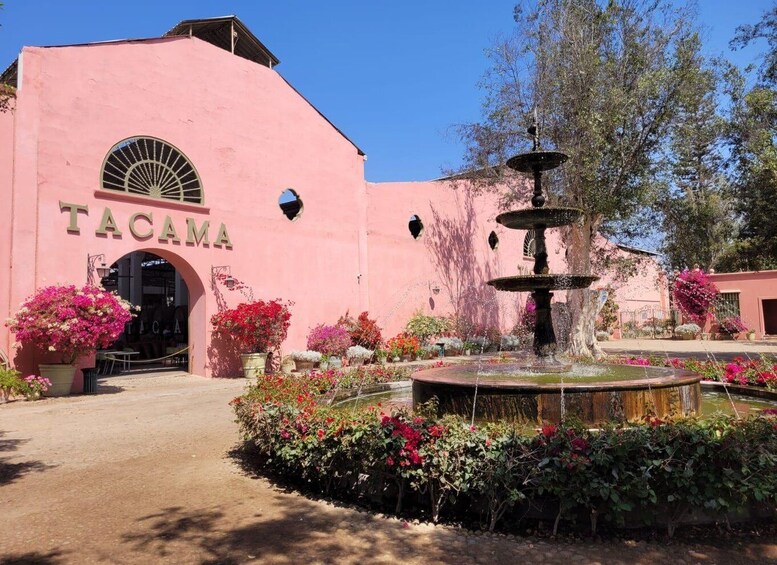 A pink building with the sign 'TACAMA' and a fountain in the foreground. 1