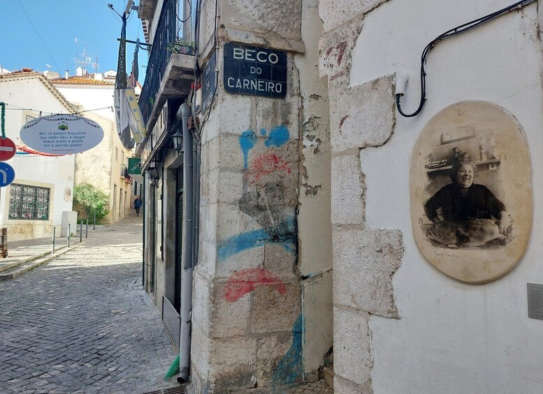 A narrow street with a sign reading "BECO DO CARNEIRO" and a mural of a person. 4