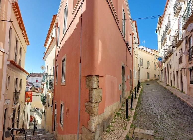 A narrow cobblestone street flanked by buildings with a pink facade and traditional architecture. 2