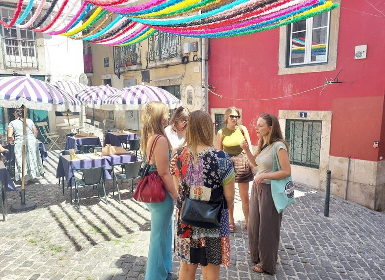 A group of people standing outdoors, a red building, and tables with umbrellas. 3