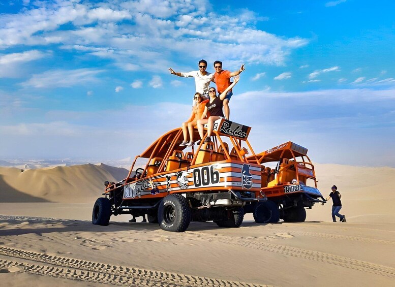 A dune buggy with people on top, desert dunes, and a clear sky. 2
