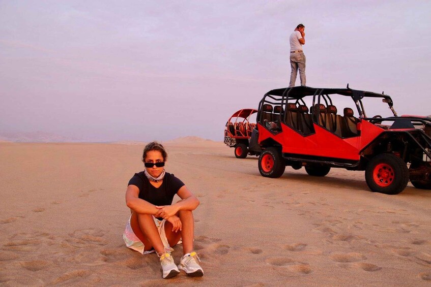 A person sitting on the sand with a red off-road vehicle in the background. 4