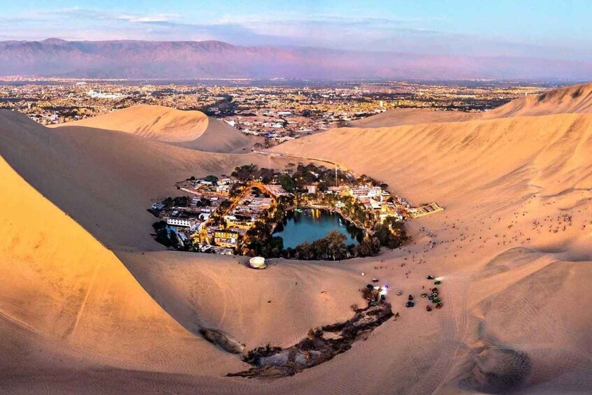 A desert landscape with sand dunes and a small settlement with buildings and a lake. 3