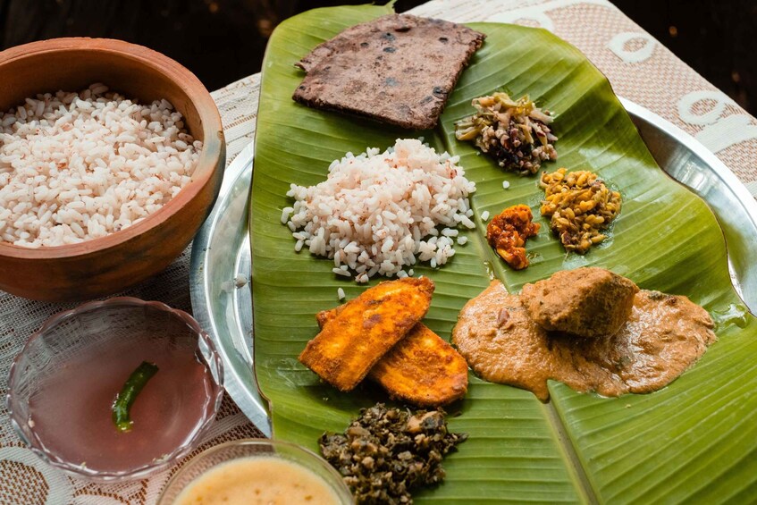 A traditional South Indian meal served on a banana leaf with rice, a meat dish, and various chutneys. 1