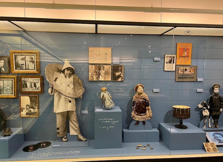 A museum exhibit with vintage photographs, dolls, and historical documents. 1