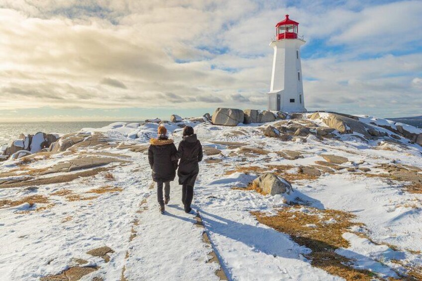 Two people walking on a snow-covered path towards a lighthouse. 2