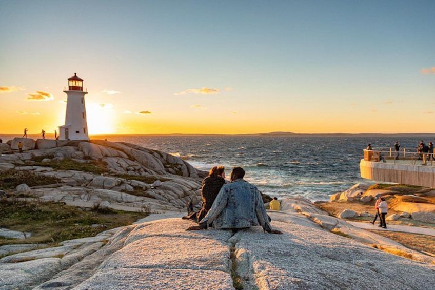A couple sitting on rocks overlooking the ocean with a lighthouse in the background. 1