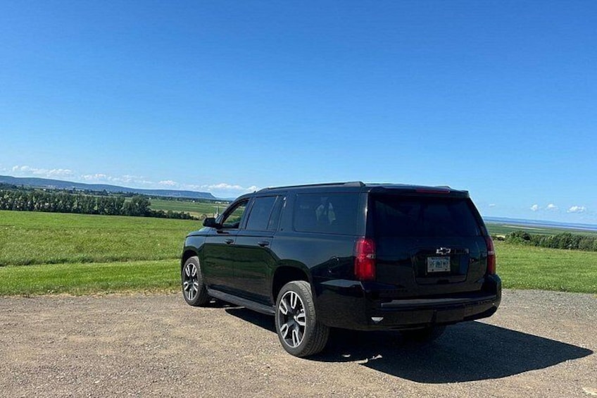 Ein schwarzer SUV auf einem Kiesgrund, mit blauem Himmel und grünen Feldern im Hintergrund. 4