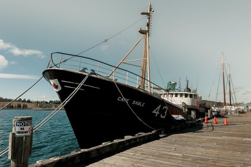 Een zwarte boot genaamd 'CAPE SABLE' ligt aangemeerd aan een houten steiger, nabij een bord met de tekst 'ROKEN VERBODEN'. 1