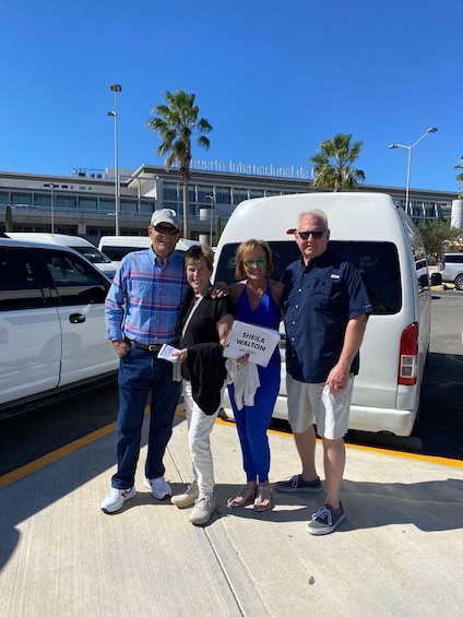 Four people standing in front of a white van with palm trees and a building in the background. 3