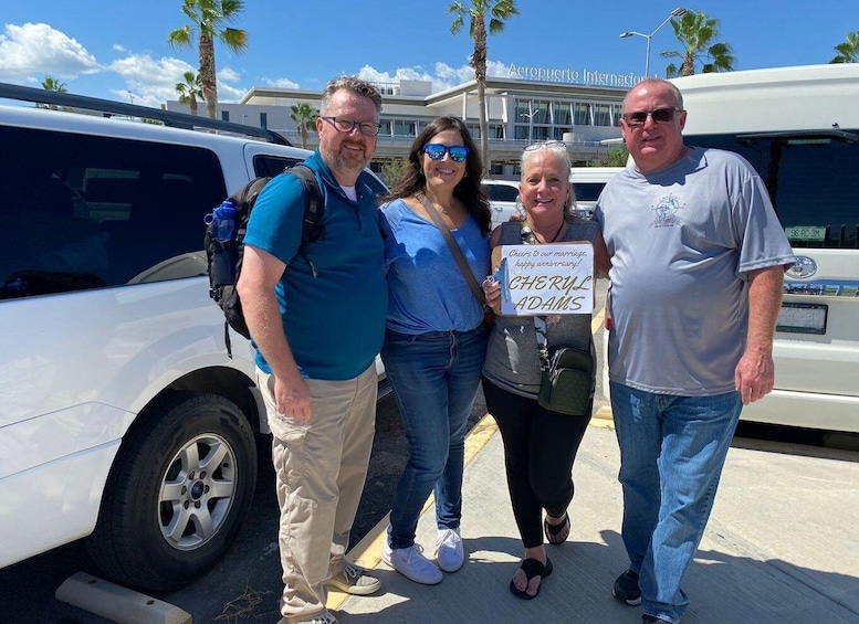 Four people standing in front of a white van with palm trees and a building in the background. 2