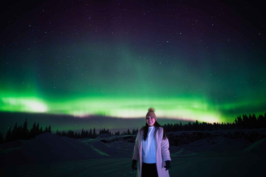 A person standing in a snowy landscape with the Northern Lights in the background. 3