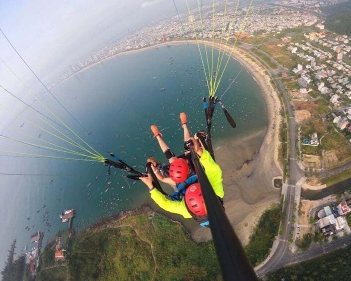 A person paragliding over a coastal area with a beach and residential buildings below. 5