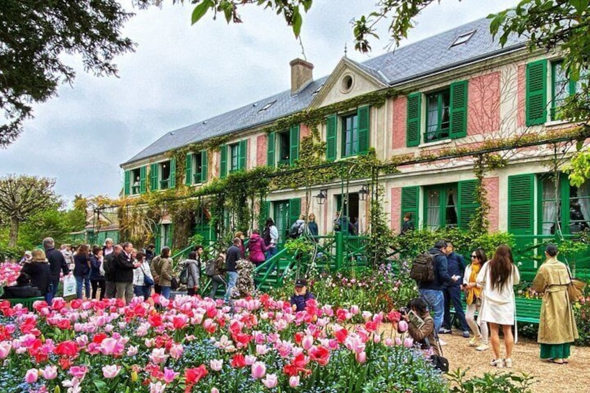 A garden with pink and red tulips in front of a building with green shutters. 4