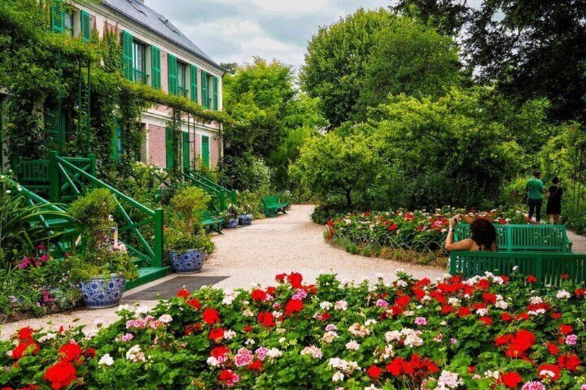 A garden with a pathway, green benches, and flowering plants. 1