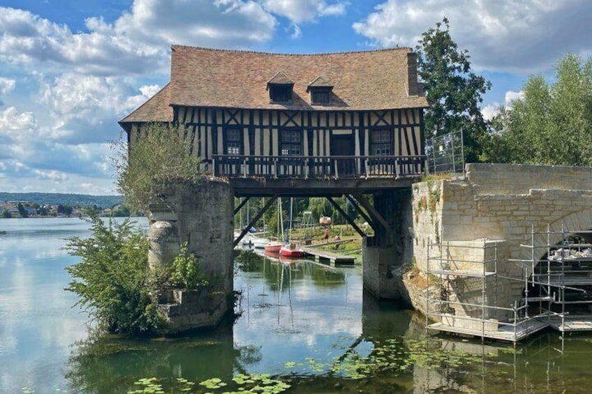 A historic building with a timber-framed structure, a stone bridge, and a calm river with boats. 1