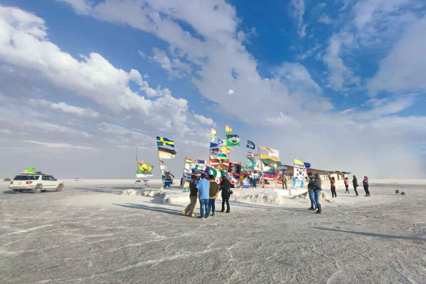 A desert landscape with a group of people standing near a structure displaying various national flags. 1