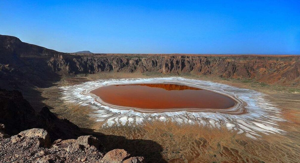 A large salt flat with a central pond surrounded by white salt deposits. 1