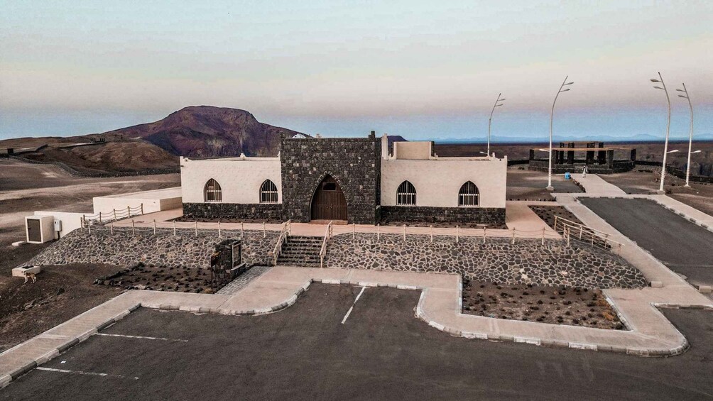 A building with a stone facade and arched windows, surrounded by a paved area and a mountainous backdrop. 2