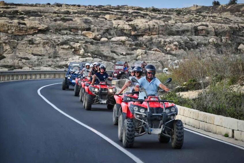 A group of people riding red ATVs on a winding road with rocky terrain and sparse vegetation in the background. 5