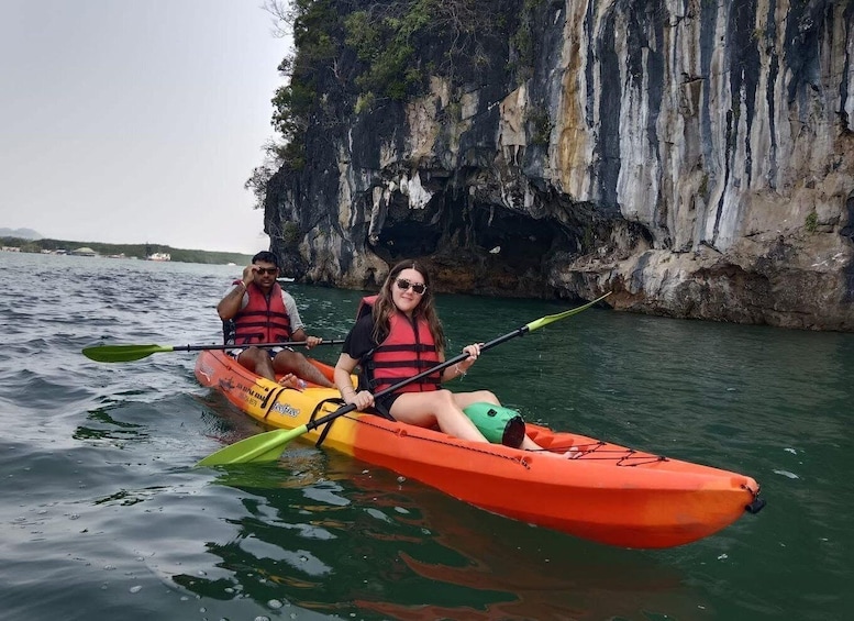 Two people kayaking in a narrow waterway with rocky cliffs on one side. 1