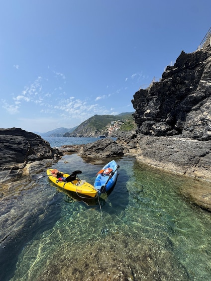 Kayaks tied to rocks in a clear shallow water area with a rocky coastline and distant buildings. 4
