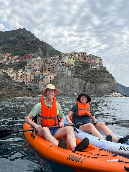 Two people kayaking on a river with colorful buildings on a hillside in the background. 5