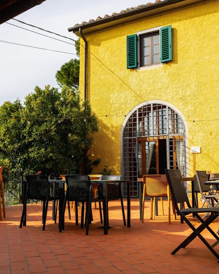 A yellow building with green shutters, outdoor seating, and a tiled patio. 2