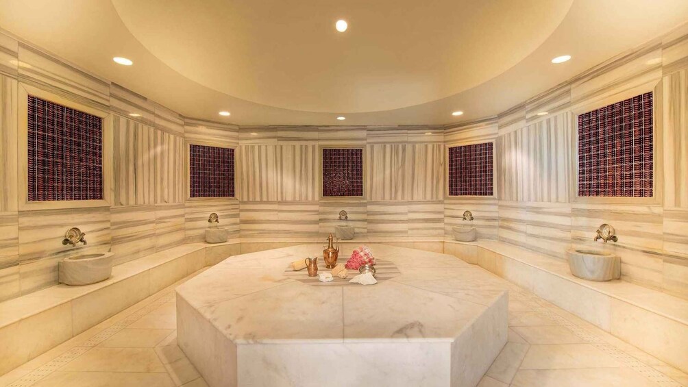A luxurious bathroom with a large marble bathtub, decorative vases, and a unique window design. 1