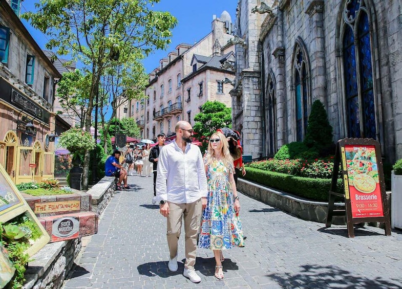 A couple walking on a cobblestone street with historic buildings and a fountainhead sign. 2