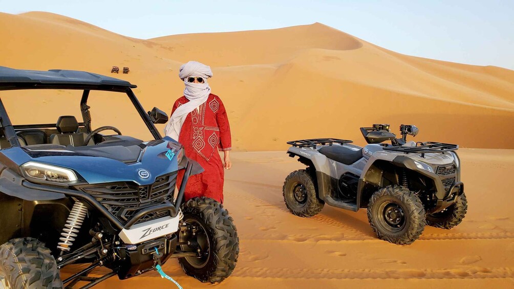 A desert landscape with sand dunes, a blue off-road vehicle, and a grey ATV. 2