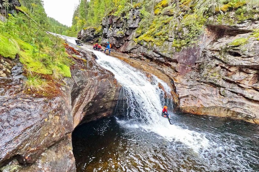 A waterfall in a forested area with people kayaking. 3