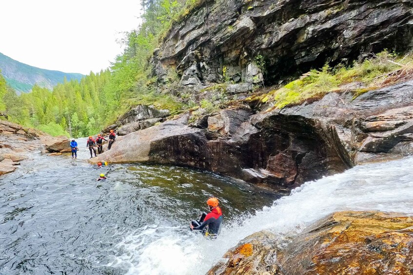 A group of people kayaking on a river surrounded by rocky cliffs and greenery. 2