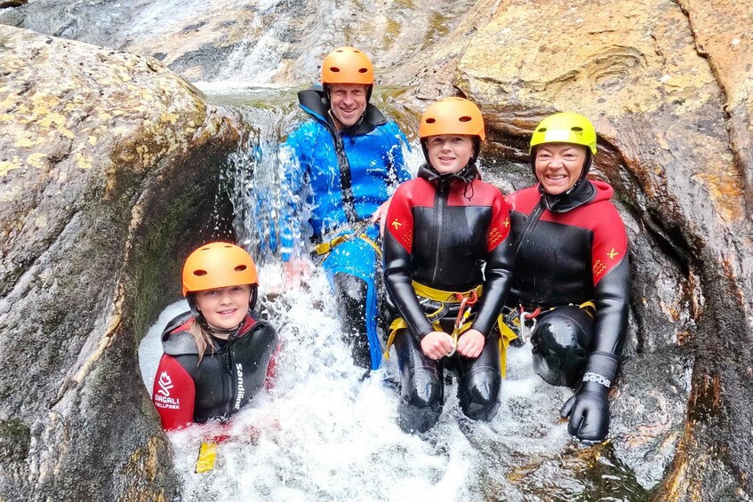 Four people in wetsuits and helmets sitting in a water-filled crevice. 5