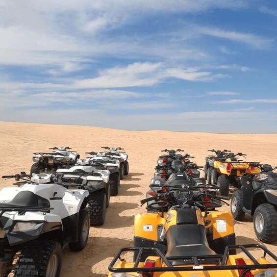 A row of ATVs parked on a sandy desert landscape under a clear sky. 1