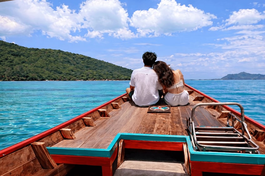 A couple on a wooden boat with turquoise water and a green hill in the background. 3