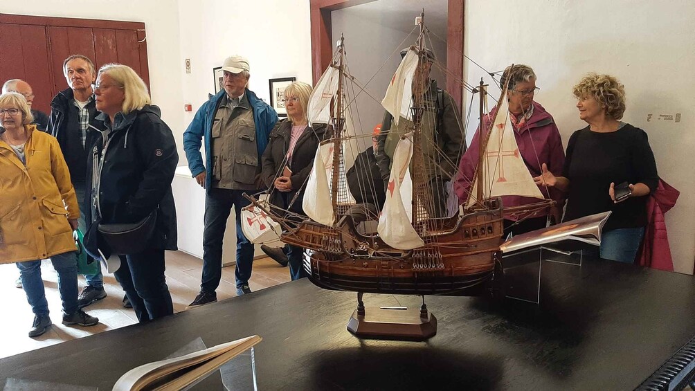 A model ship displayed on a table with people observing it. 4