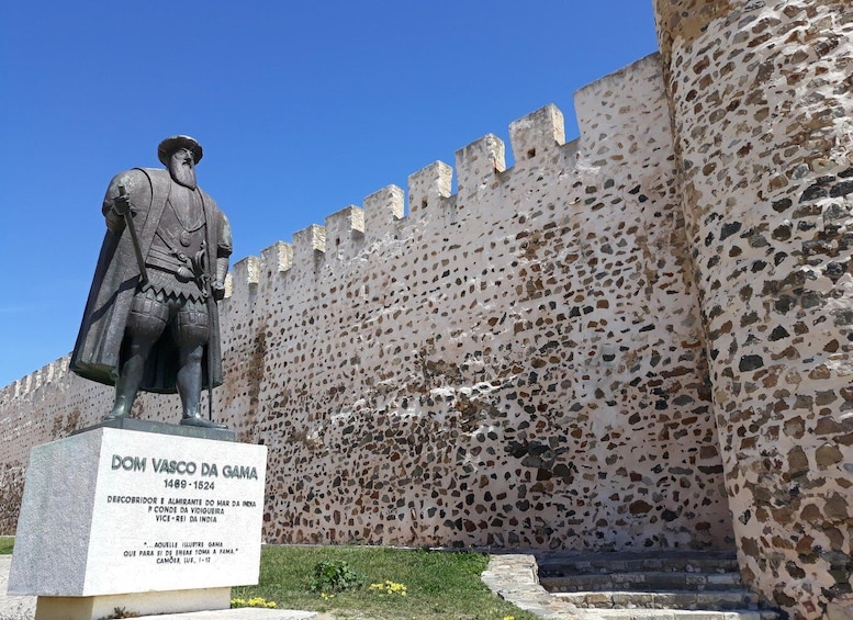 A statue of Vasco da Gama with a plaque, set against a stone wall. 1
