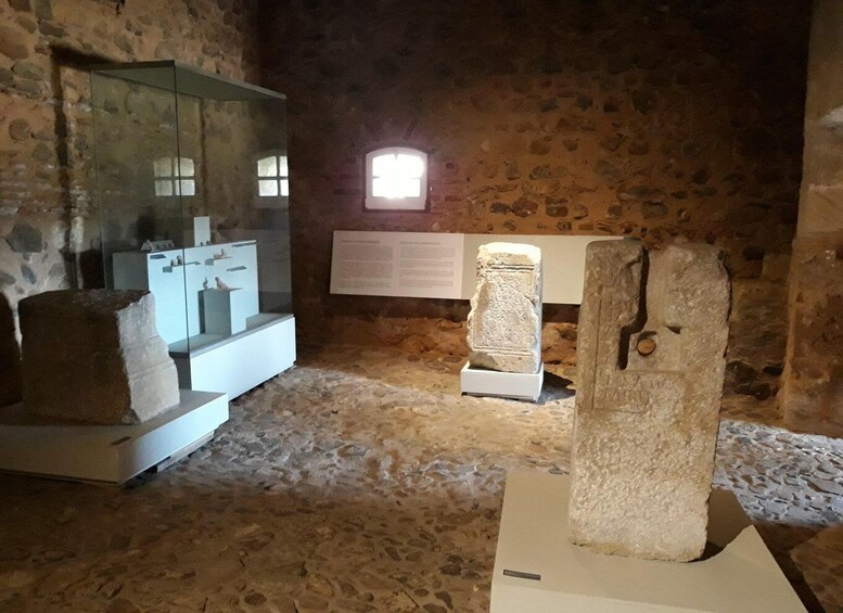 An ancient stone room with a stone wall, a window, and a display case with artifacts. 3