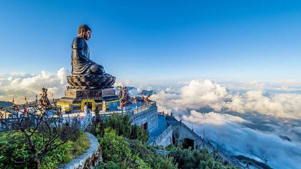 A large Buddha statue on a mountain peak with a view of clouds below. 2