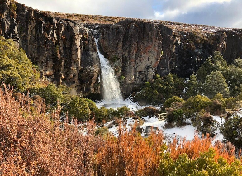 A waterfall cascading down a rocky cliff surrounded by autumn foliage and snow patches. 5