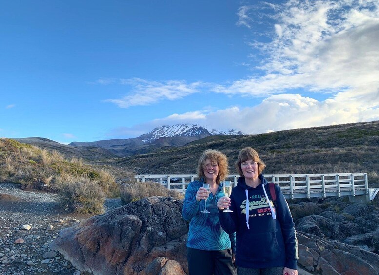 Two people toasting with champagne glasses in a rocky outdoor setting with a mountain in the background. 1