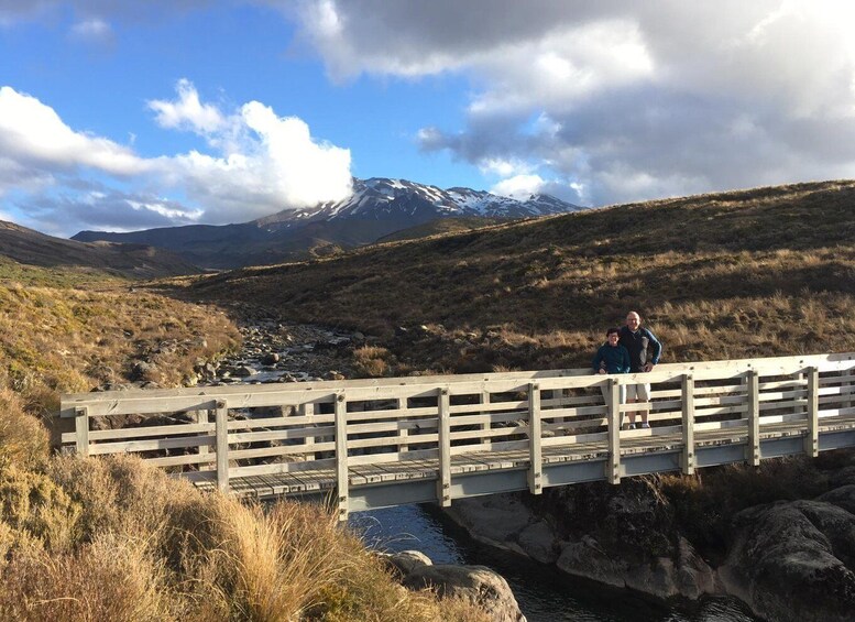 A wooden bridge over a stream in a mountainous area with a person standing on it. 3