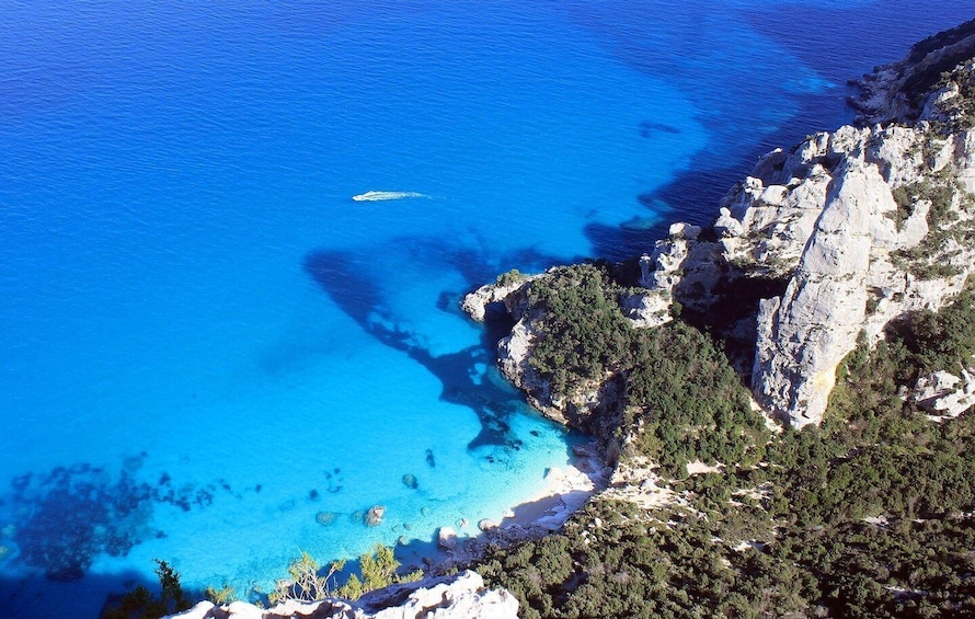 A coastal landscape with clear blue waters, rocky cliffs, and dense greenery. 1