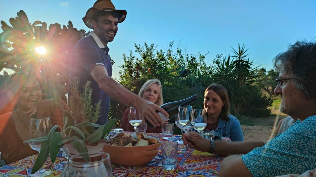A group of people at a table with a colorful tablecloth, enjoying a meal outdoors with a sunny sky in the background. 4