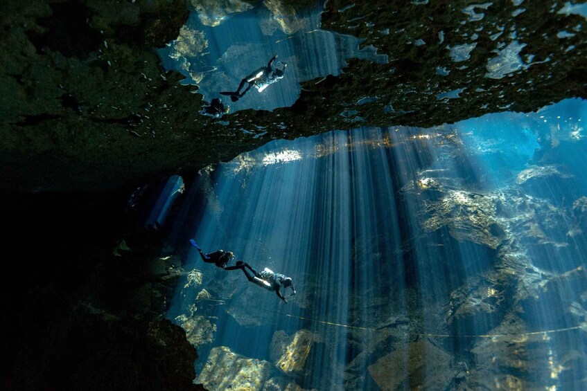Dos buzos bajo el agua en una cueva, con rayos de sol filtrándose. 2